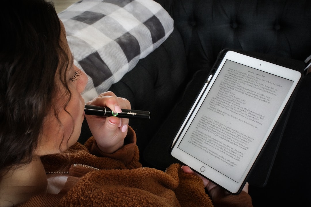 A young woman reading a digital tablet puffs on a black Dip Devices Lunar cannabis concentrate vape. Get yours at https://dipdevices.com/