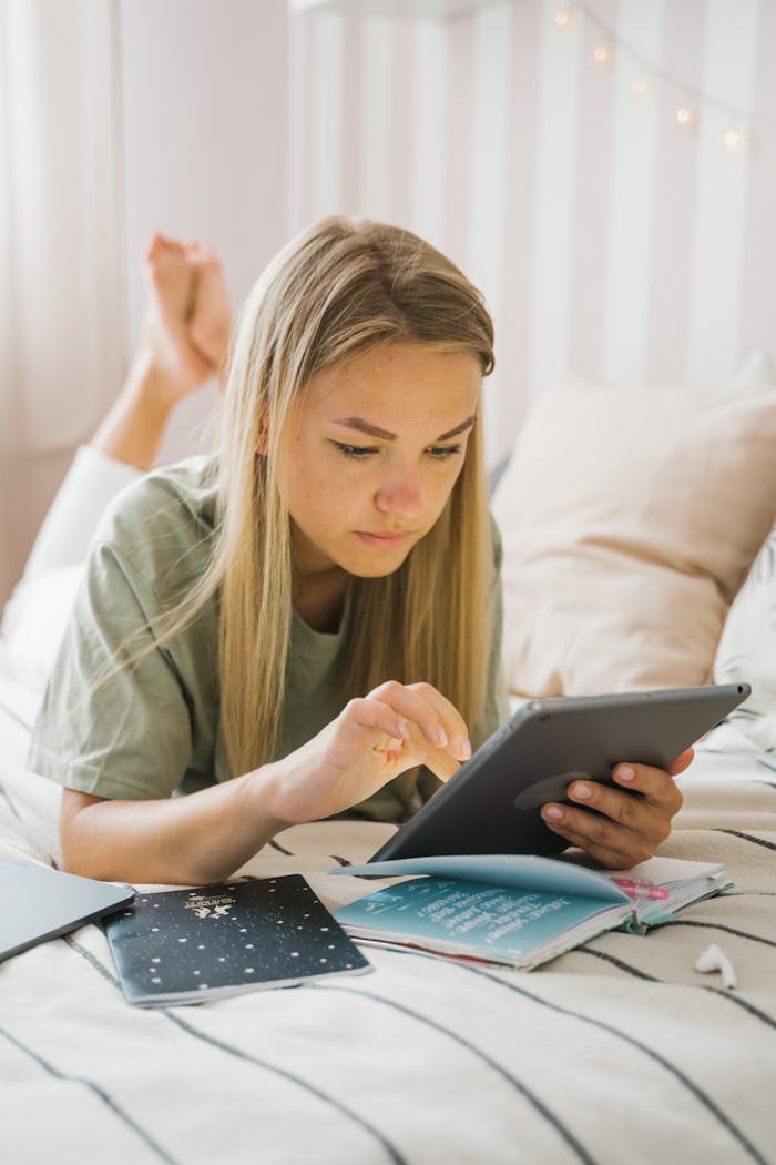 Young woman lying on bed using a tablet in a cozy bedroom setting. Ideal for lifestyle content.